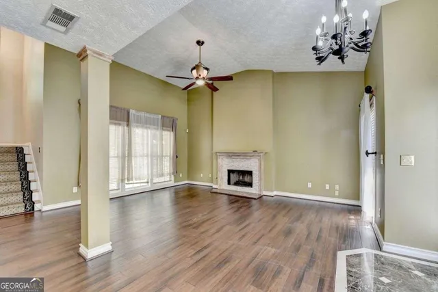 an empty room with wooden floor chandelier fan and windows