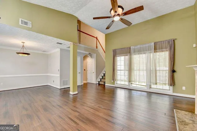 an empty room with wooden floor fan and windows