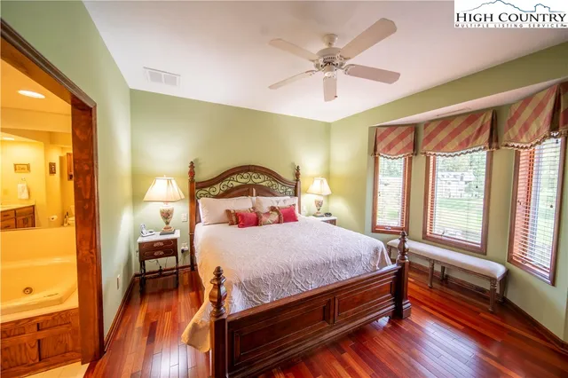 a bedroom with a bed a chandelier and a large window with wooden floor