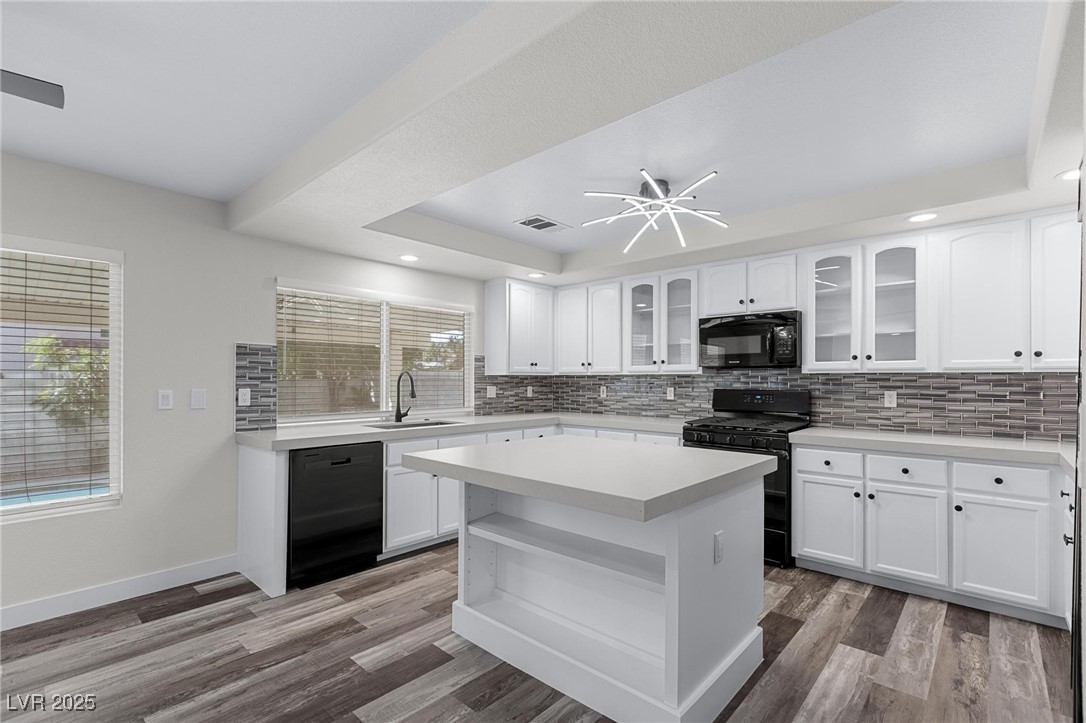 9591 Antelope Bend Court Las Vegas, NV 89148 - Photo 12 of 56 Kitchen with a tray ceiling, black appliances, glass insert cabinets, white cabinetry, and center island