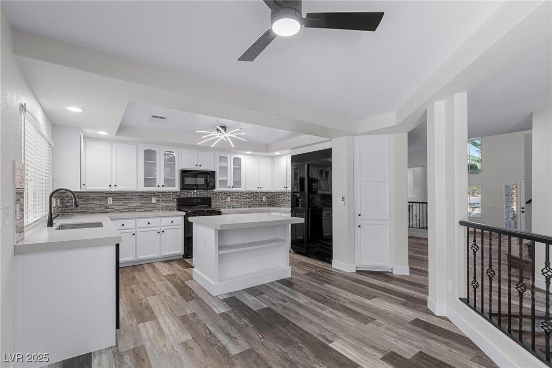 9591 Antelope Bend Court Las Vegas, NV 89148 - Photo 13 of 56 Kitchen with a tray ceiling, black appliances, glass insert cabinets, white cabinetry, and center island