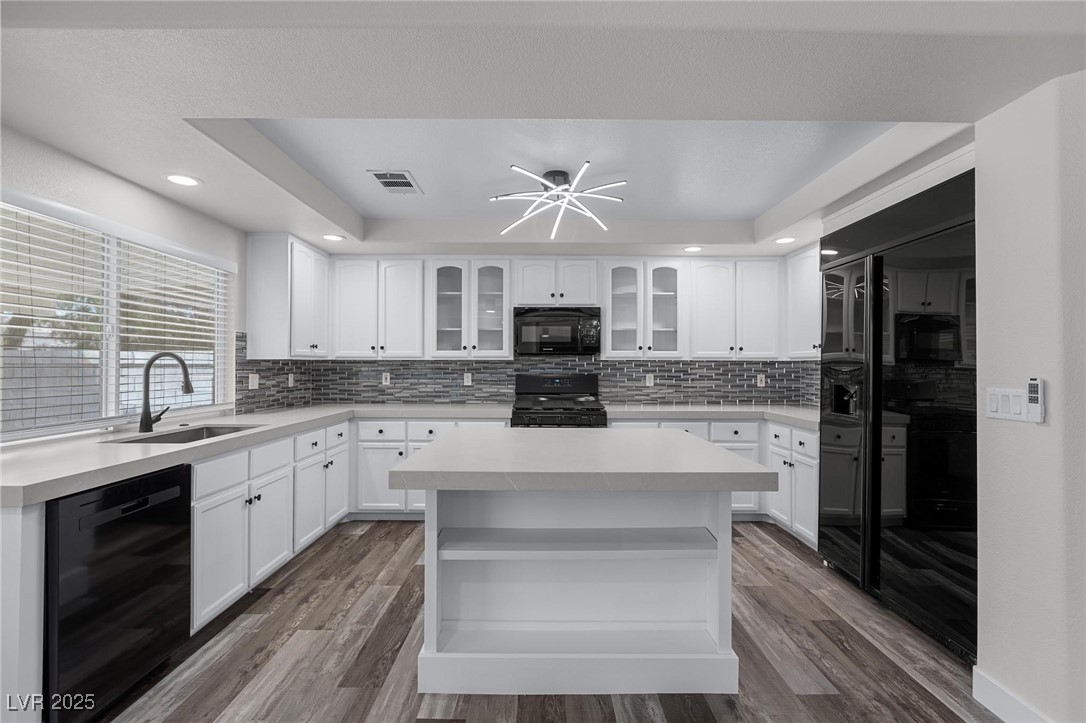 9591 Antelope Bend Court Las Vegas, NV 89148 - Photo 14 of 56 Kitchen with a tray ceiling, black appliances, glass insert cabinets, white cabinetry, and center island