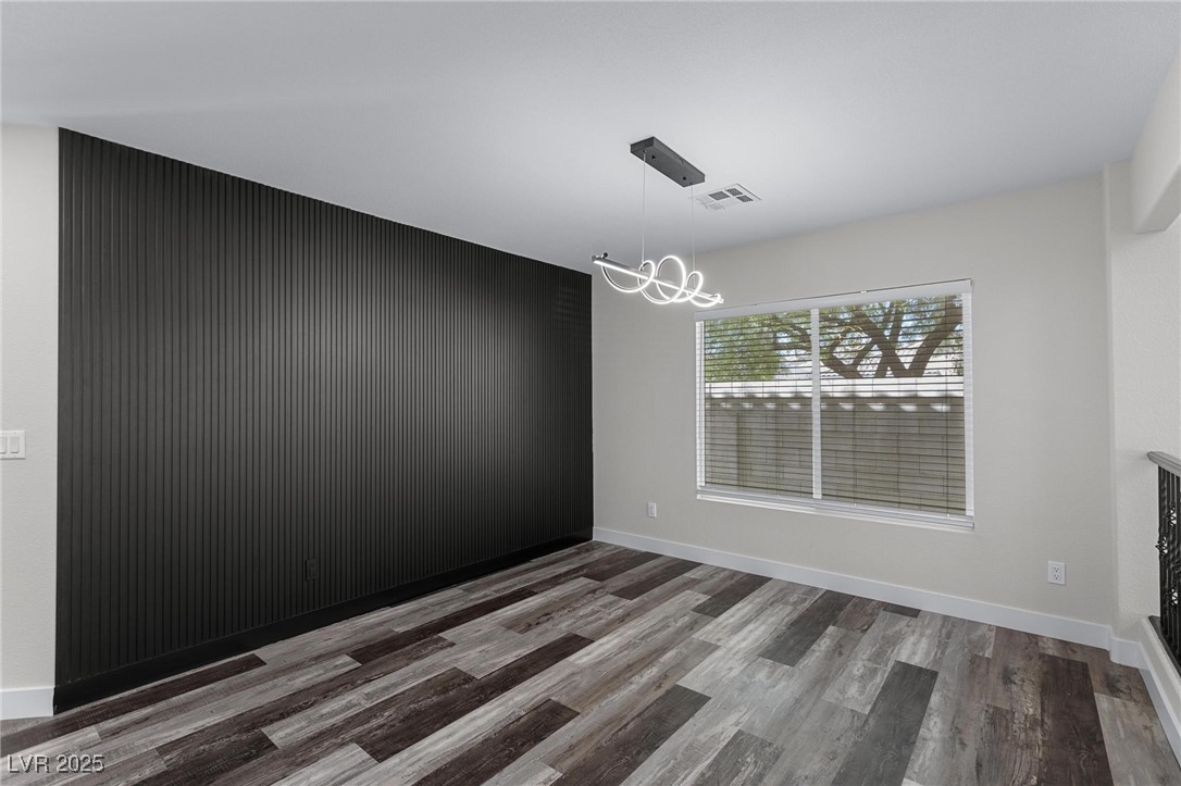 9591 Antelope Bend Court Las Vegas, NV 89148 - Photo 9 of 56 Unfurnished dining room featuring dark wood finished floors, a chandelier, and an accent wall