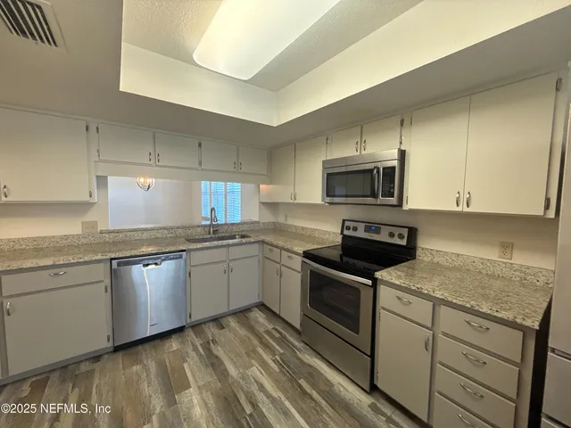 a kitchen with granite countertop a sink dishwasher stove and microwave with wooden floor