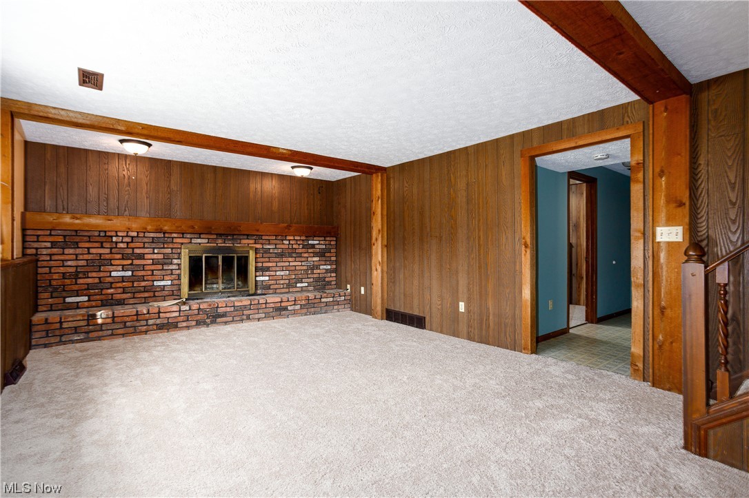5680 Lance Road Medina, OH 44256 - Photo 20 of 32 Unfurnished living room featuring light carpet, a textured ceiling, beam ceiling, wooden walls, and a fireplace