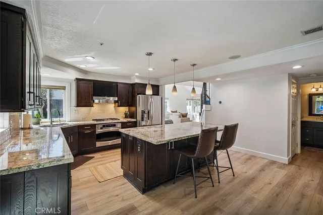 a kitchen with stainless steel appliances kitchen island granite countertop a table chairs sink and cabinets