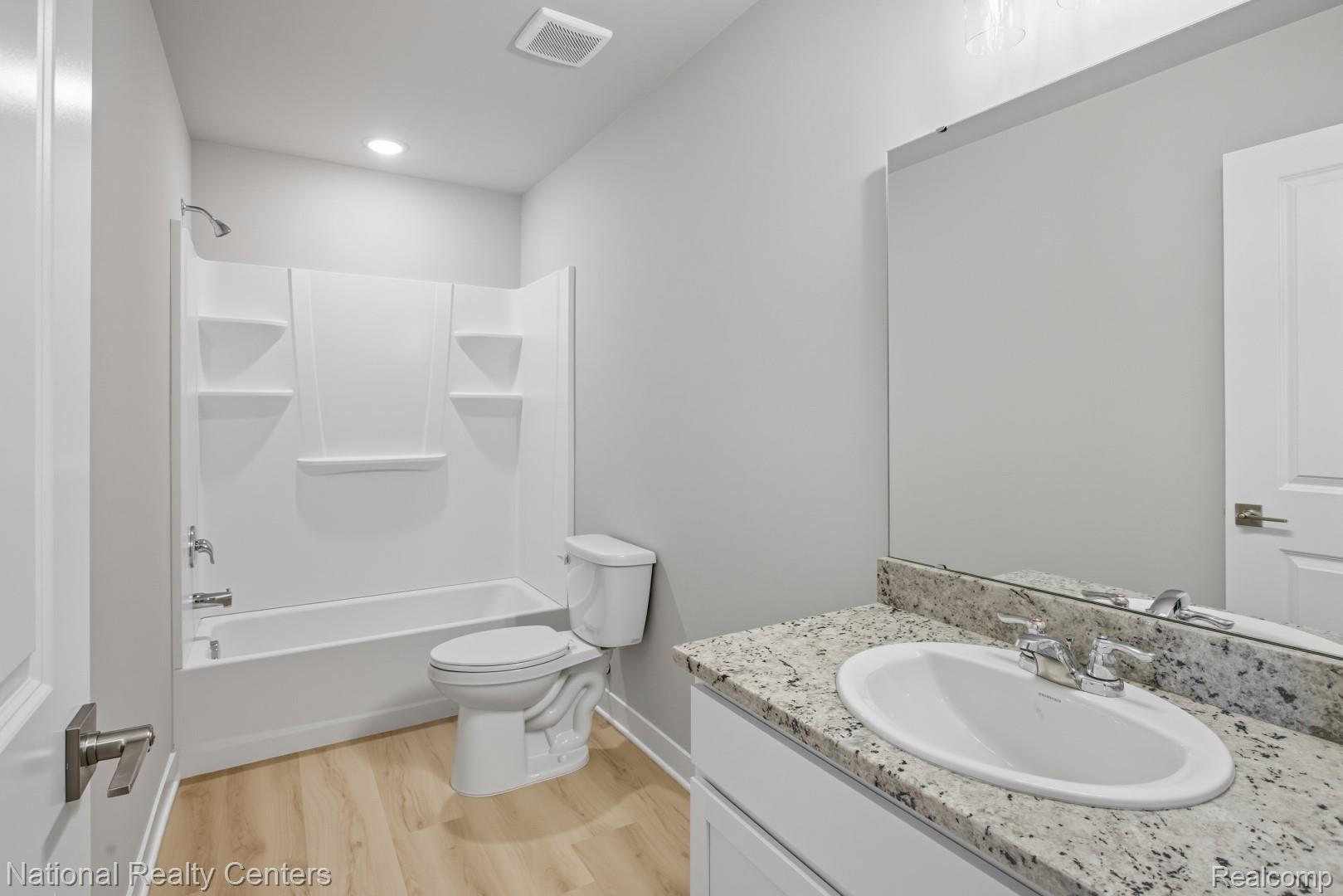 25018 Reeck Road Trenton, MI 48183 - Photo 26 of 32 Bathroom featuring a tub/shower combination, light wood-finish flooring, a toilet, a vanity with an undermount sink, and a framed mirror