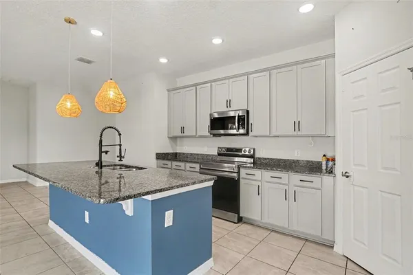 a kitchen with kitchen island granite countertop a sink a stove a counter space and cabinets