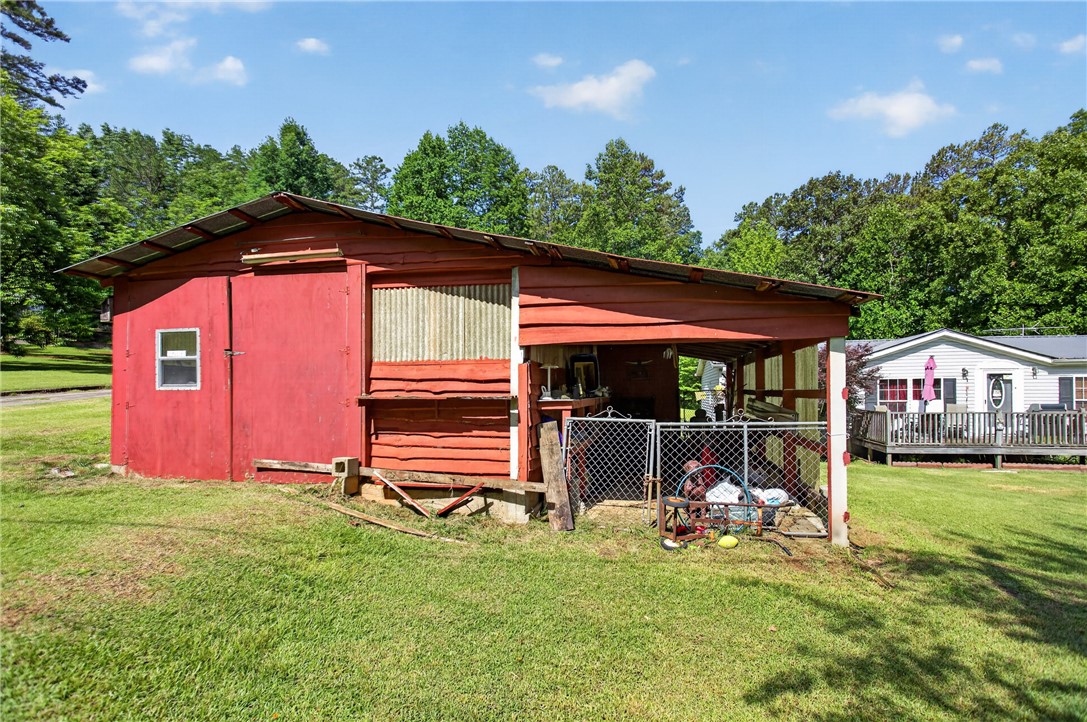 418 Chauga Road Westminster, SC 29693 - Photo 23 of 38 A rustic red shed offers ample storage space, complemented by a vibrant green lawn and distant foliage.