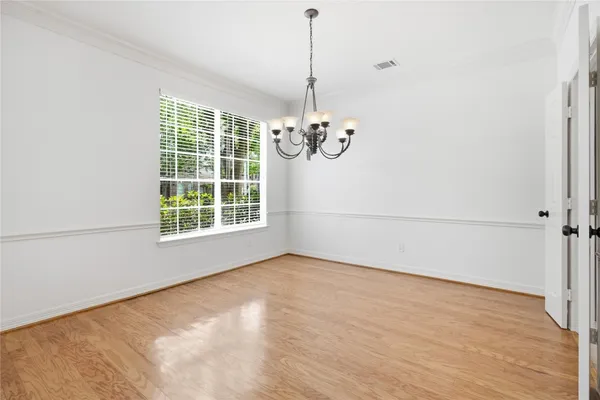 an empty room with a chandelier fan and wooden floor