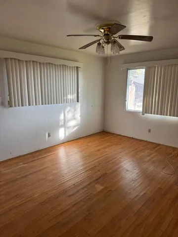 an empty room with wooden floor fan and windows