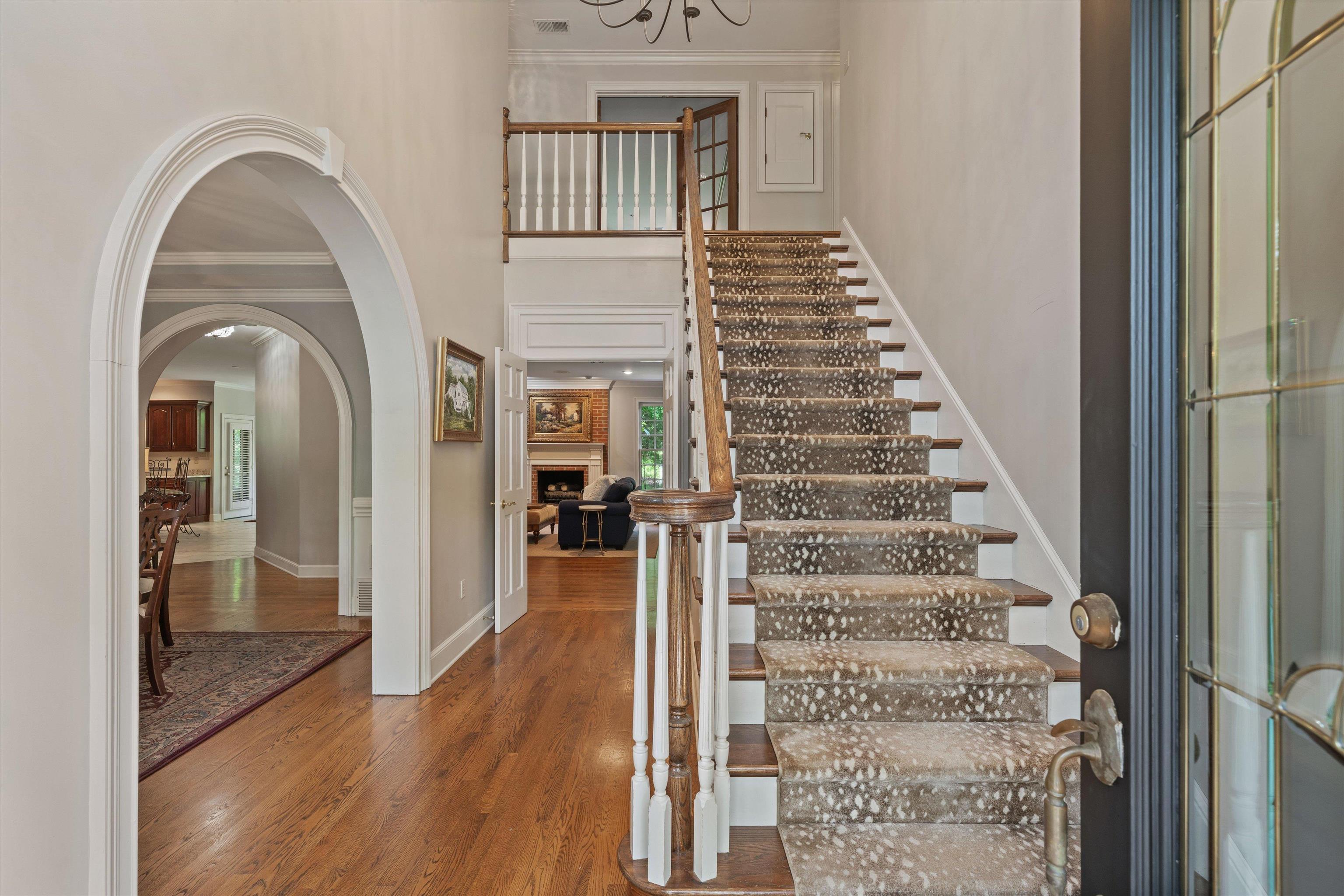 8897 Forest Ridge Cove Memphis, TN 38018 - Photo 3 of 35 Staircase with wood finished floors, a towering ceiling, ornamental molding, a fireplace, and arched walkways