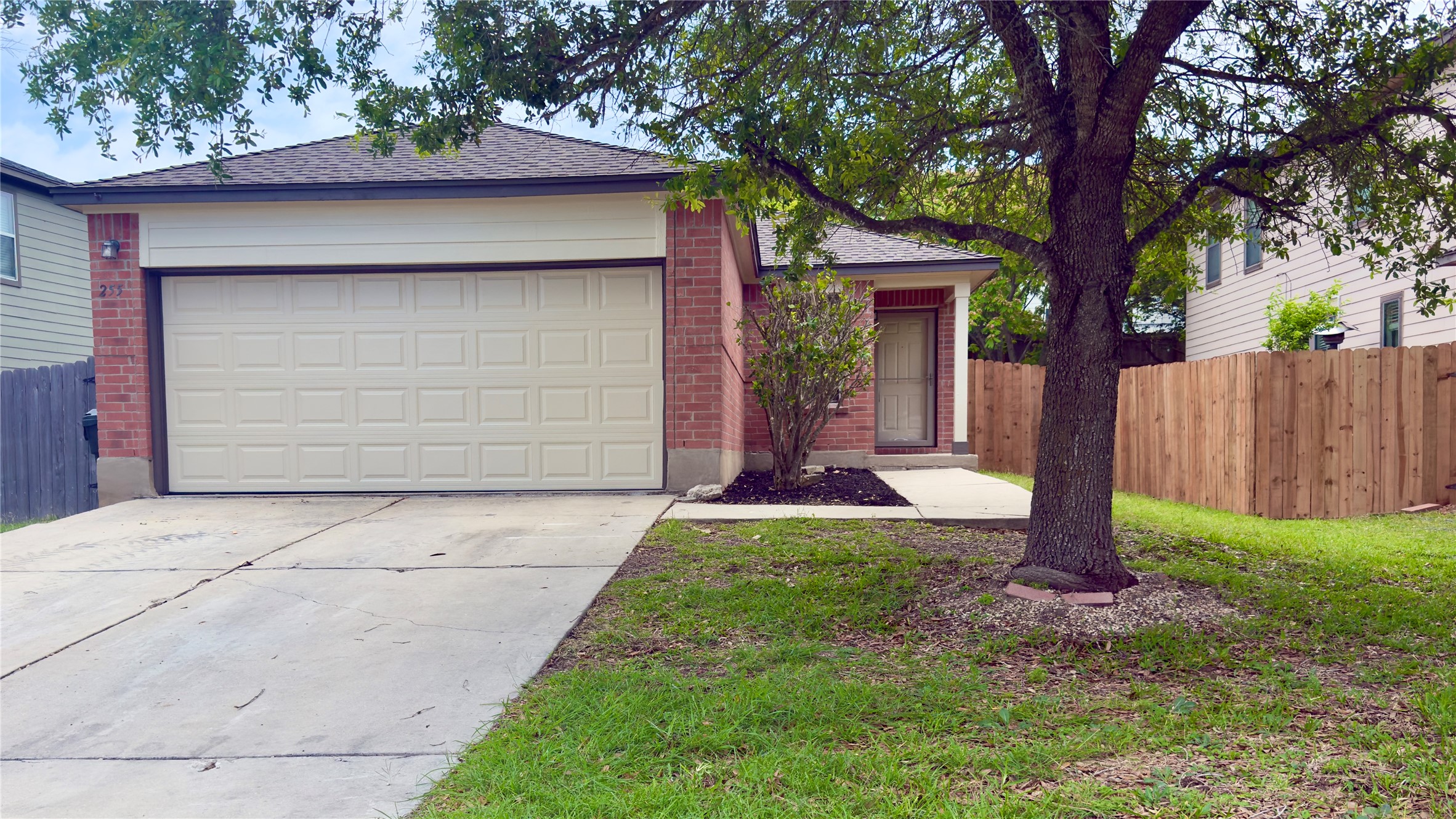 255 Myrtle Street Kyle, TX 78640 - Photo 1 of 31 Brick facade residence featuring an attached garage with a panel door, a concrete driveway, a sidewalk entrance, and a privacy fence