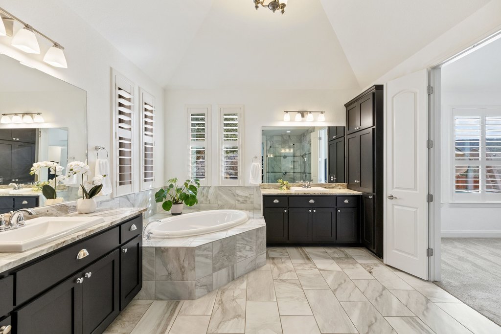 5812 Davenport Divide Road Austin, TX 78738 - Photo 22 of 40 Black cabinetry contrasts beautifully with the marble tile flooring and surround. The soaking tub is framed in stone beneath shuttered windows, and dual vanities offer generous counter space and storage. Clean lines, elevated finishes, and plenty of breathing room make this feel like a true everyday luxury.