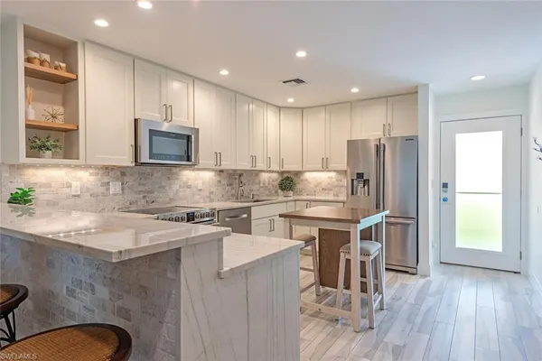 a kitchen with stainless steel appliances granite countertop a refrigerator a stove a sink a microwave a dining table and chairs with wooden floor