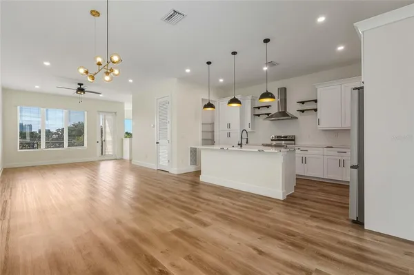 a view of an empty room and kitchen with wooden floor