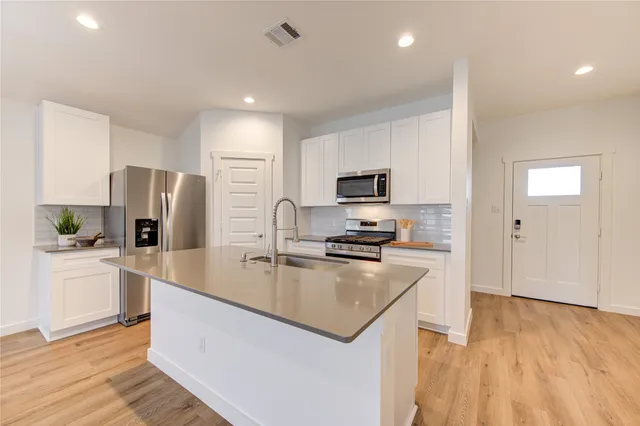 a view of an empty room with wooden floor and a kitchen