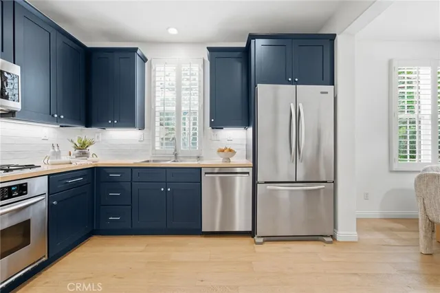 a kitchen with stainless steel appliances granite countertop a refrigerator a sink dishwasher a stove and a dining table with wooden floor