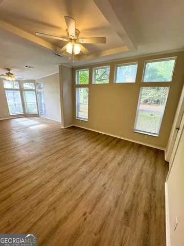 an empty room with wooden floor chandelier fan and windows