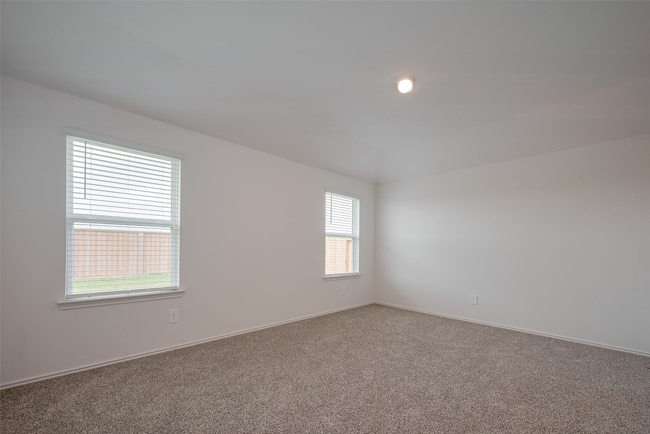30910 Rockstock Road Fulshear, TX 77441 - Photo 24 of 33 This spacious primary bedroom features a soft sloped ceiling and expansive windows that invite in the daylight. The carpeting and airy dimensions create a serene personal space.