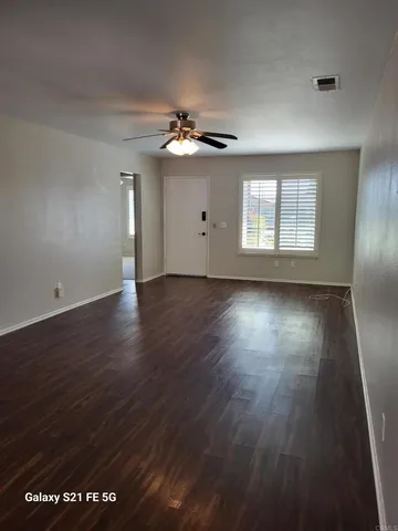 an empty room with wooden floor chandelier fan and windows