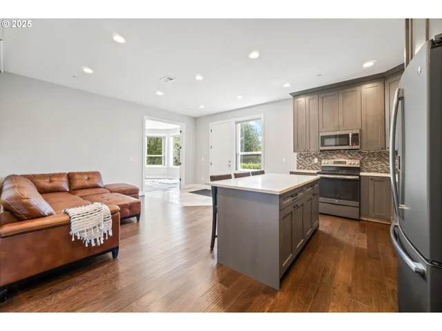 a kitchen with stainless steel appliances granite countertop a stove top oven a sink dishwasher a refrigerator and white cabinets with wooden floor