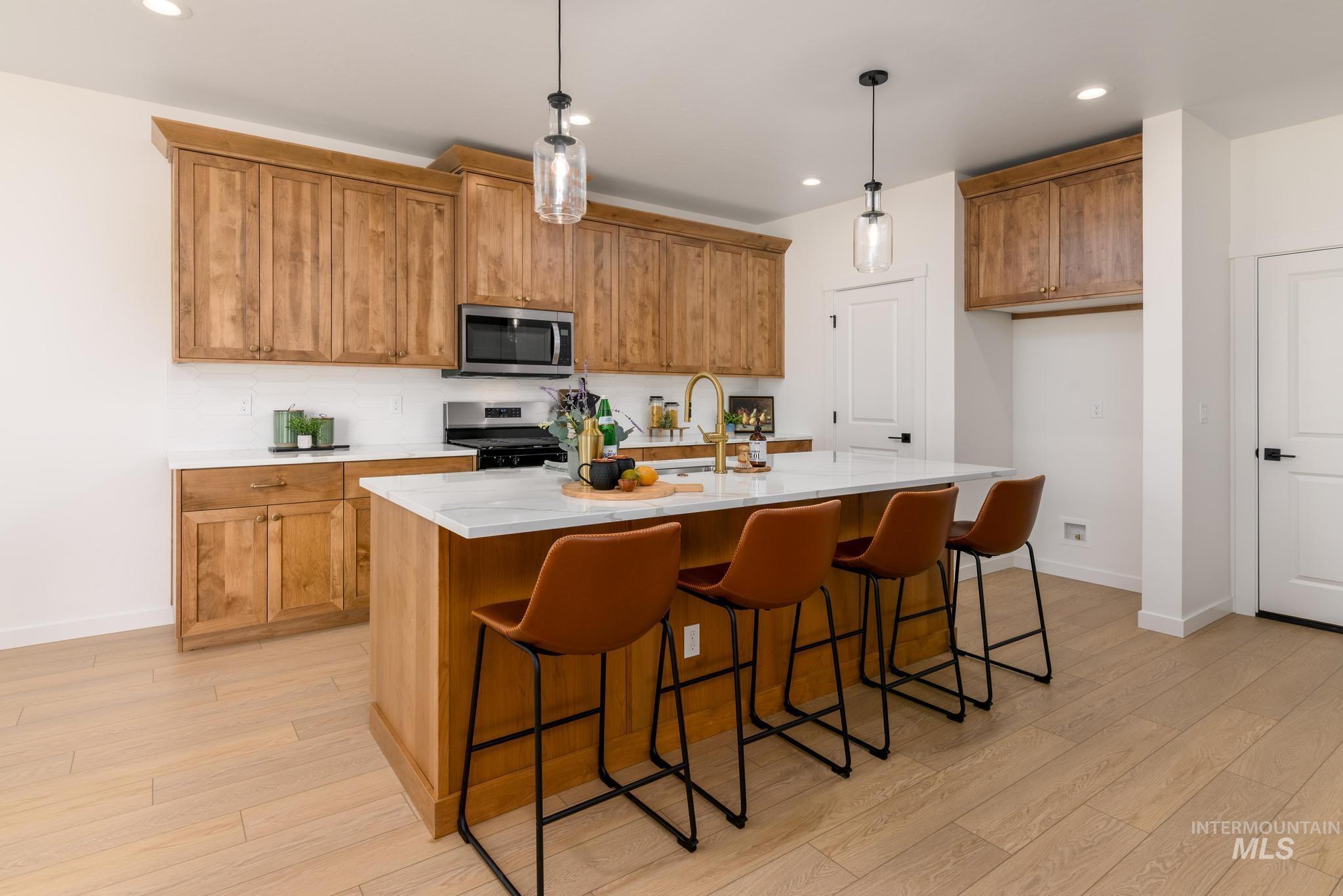 1671 West Arya Street Kuna, ID 83634 - Photo 5 of 12 Kitchen featuring a breakfast bar area, brown cabinets, light stone counters, an island with sink, and stainless steel appliances