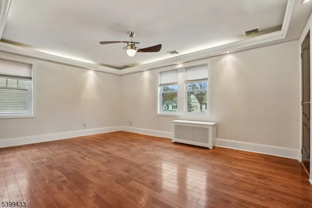 an empty room with wooden floor a ceiling fan and windows