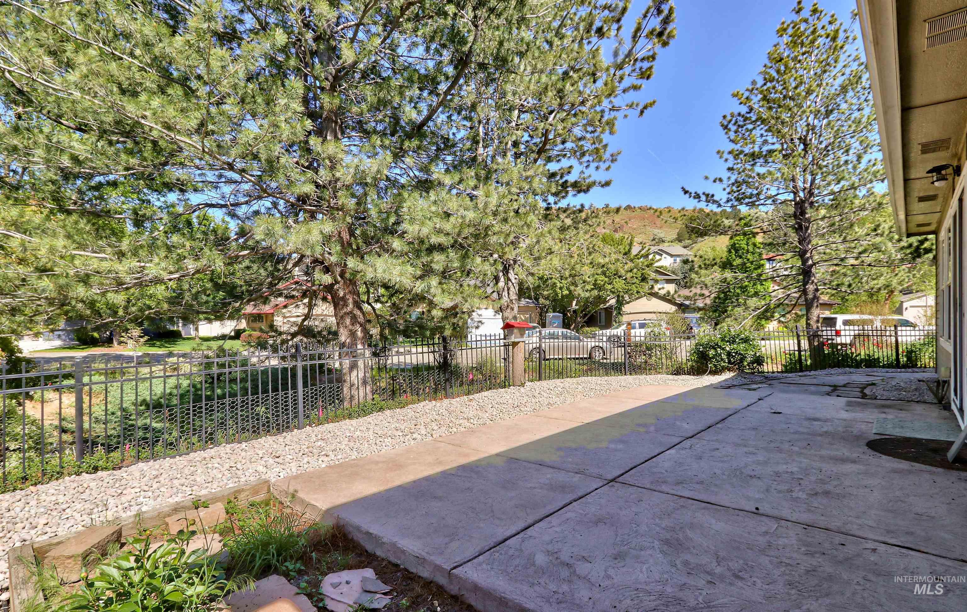 892 South Capitola Way Boise, ID 83712 - Photo 34 of 34 Concrete patio area with a gravel border, featuring a black metal fence and mature trees