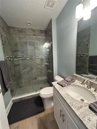 a bathroom with a granite countertop sink a toilet a mirror and shower