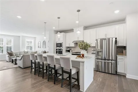 a kitchen with stainless steel appliances a refrigerator a stove a sink a dining table and chairs with wooden floor