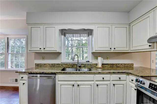 a kitchen with granite countertop a refrigerator a sink dishwasher a stove and white cabinets with wooden floor