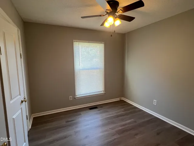 an empty room with wooden floor fan and windows