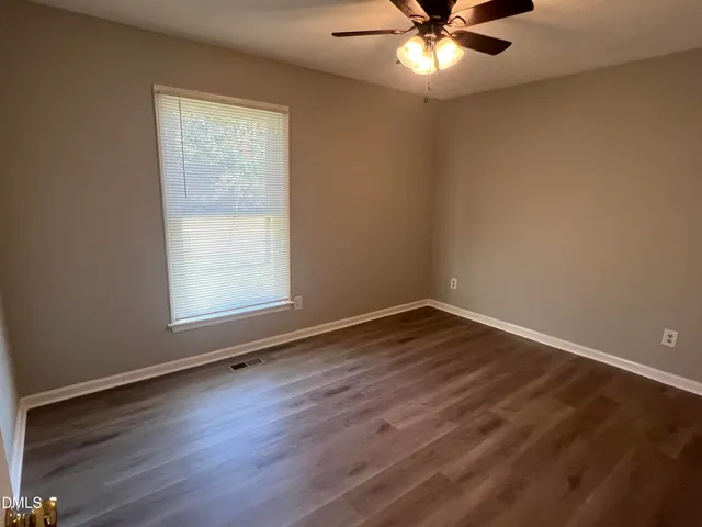 an empty room with wooden floor fan and windows