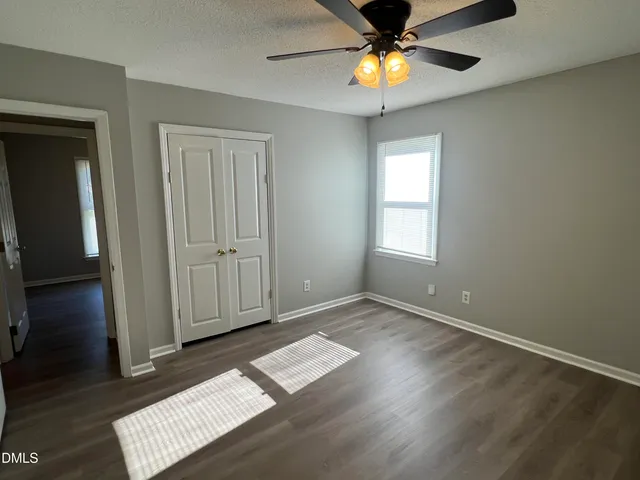an empty room with wooden floor chandelier fan and windows