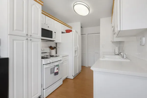 a kitchen with stainless steel appliances a white stove top oven a sink a refrigerator and white cabinets with wooden floor