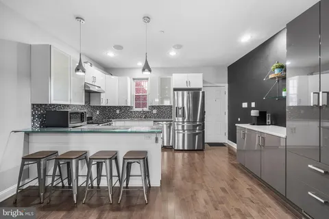 a kitchen with stainless steel appliances granite countertop a refrigerator a sink dishwasher a stove and white cabinets with wooden floor