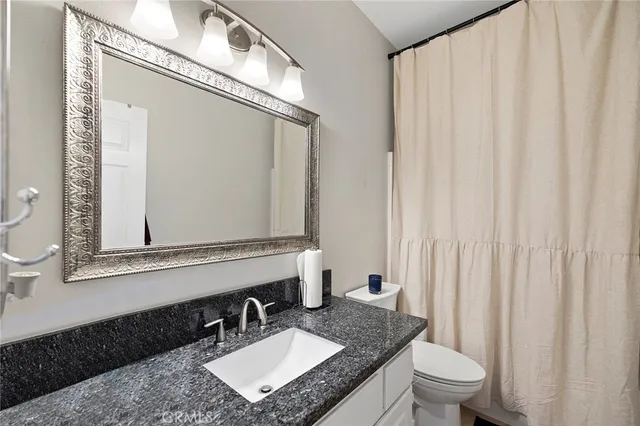 a bathroom with a granite countertop sink vanity mirror and a toilet
