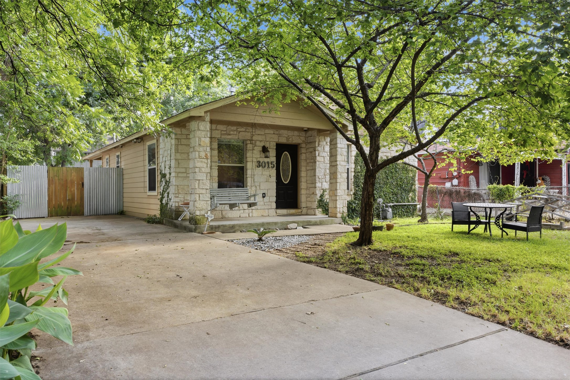 3015 Castro Street Austin, TX 78702 - Photo 2 of 40 A charming stone and siding bungalow awaits with a welcoming front porch swing and lush surrounding foliage.