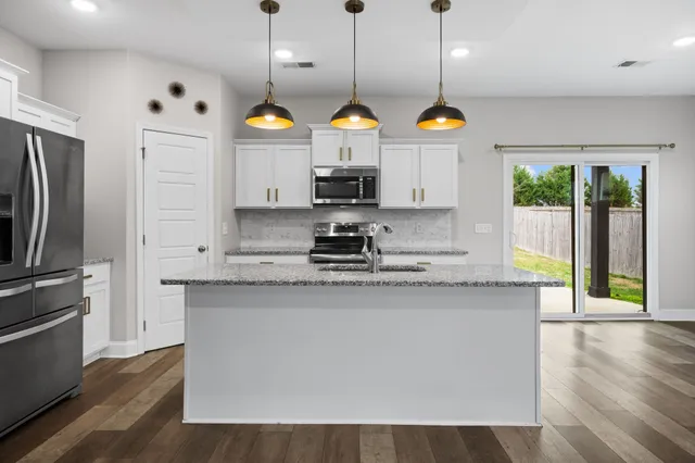 a kitchen with stainless steel appliances granite countertop a refrigerator a sink dishwasher a stove and a dining table with wooden floor