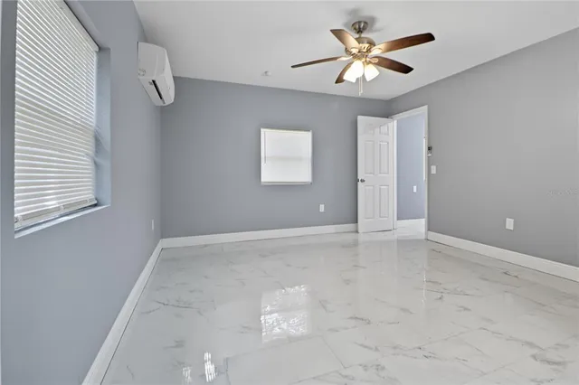 an empty room with chandelier fan and windows