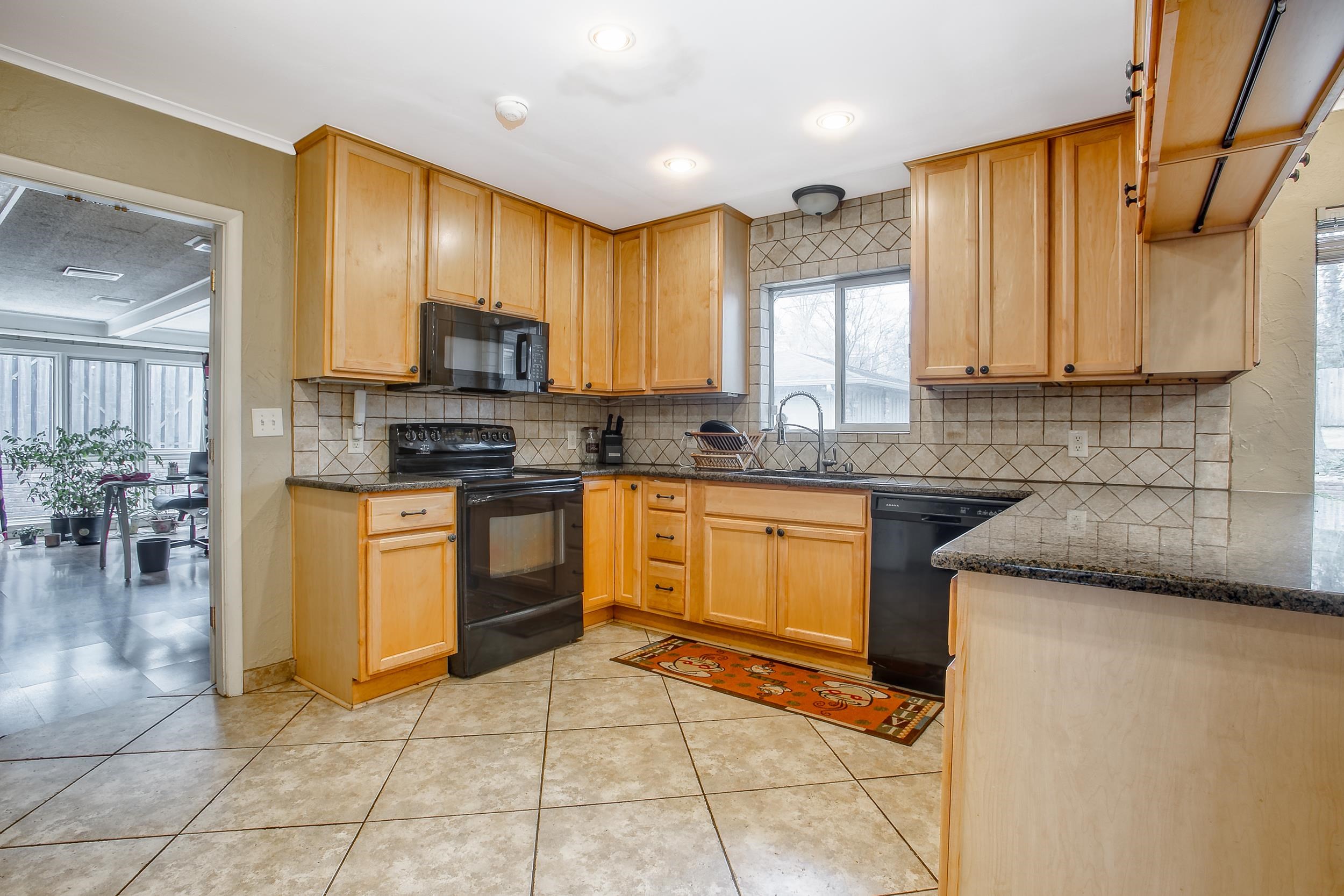 5680 North Angela Road Memphis, TN 38120 - Photo 16 of 33 Kitchen with black appliances, a sink, dark stone countertops, tasteful backsplash, and light tile patterned floors
