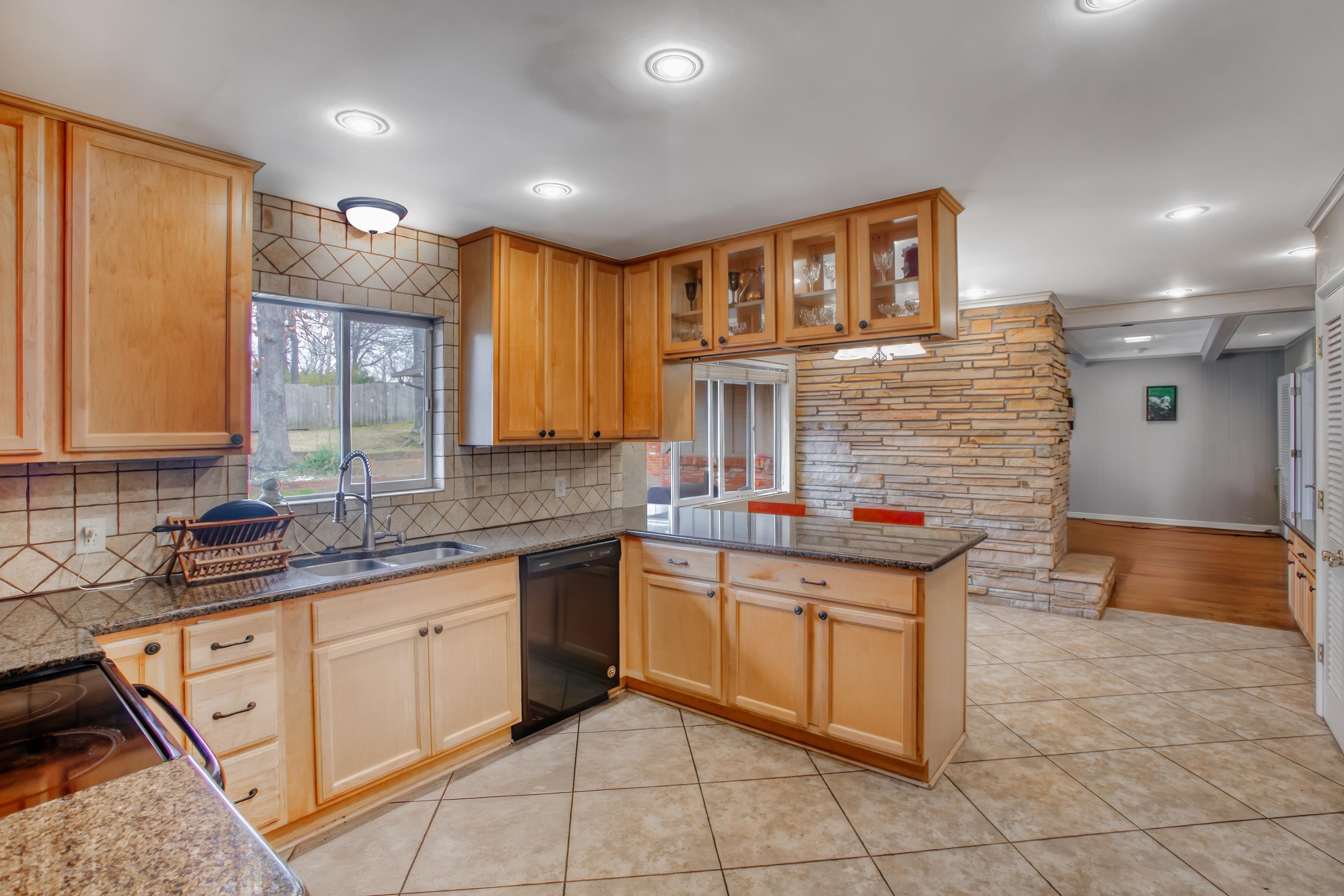 5680 North Angela Road Memphis, TN 38120 - Photo 20 of 33 Kitchen with dark stone counters, a peninsula, black appliances, glass insert cabinets, and light tile patterned floors