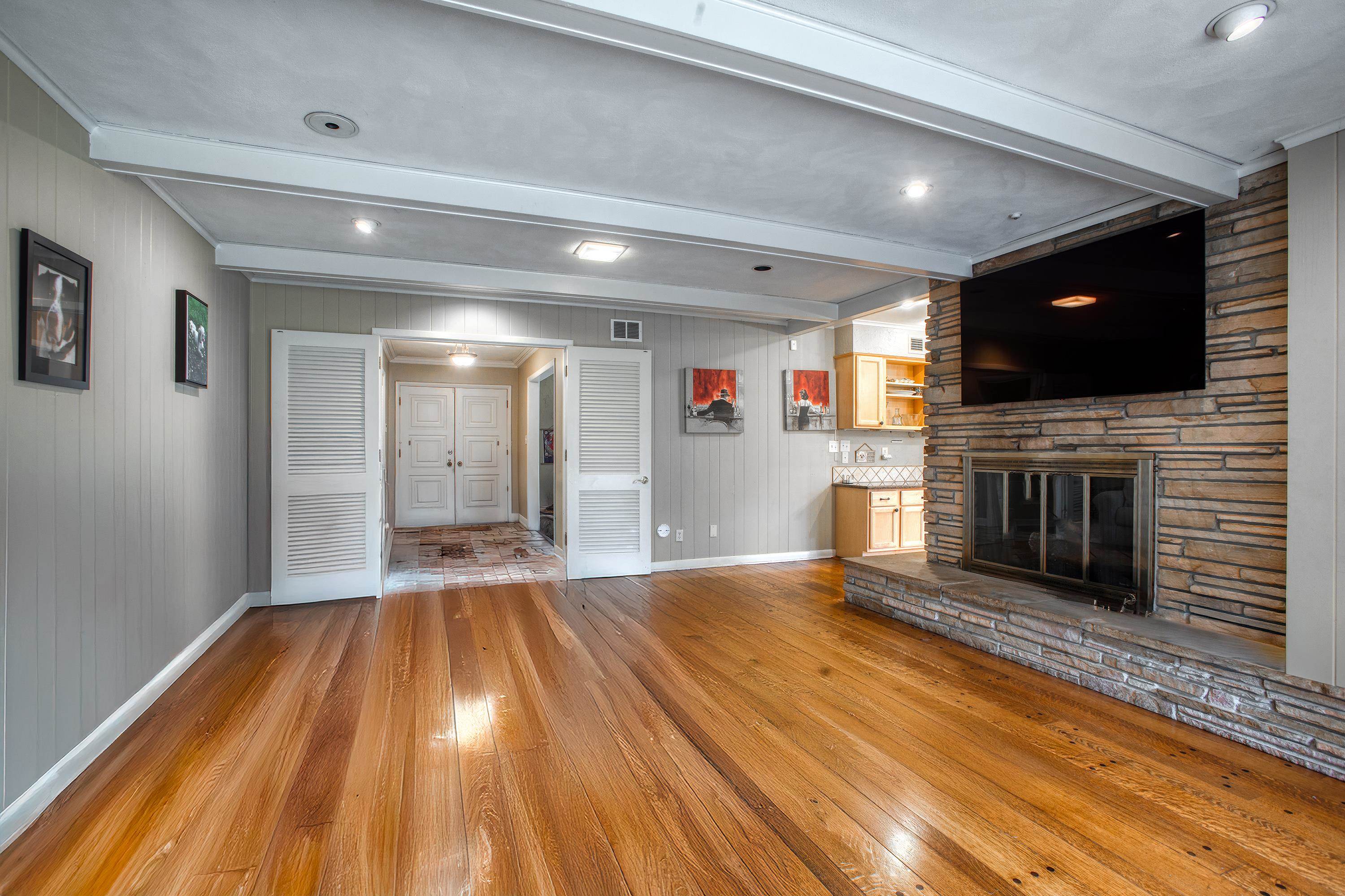 5680 North Angela Road Memphis, TN 38120 - Photo 4 of 33 Unfurnished living room featuring beam ceiling, hardwood / wood-style flooring, a stone fireplace, wood walls, and crown molding