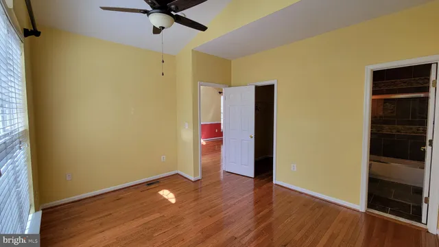 a view of an empty room with wooden floor and a ceiling fan