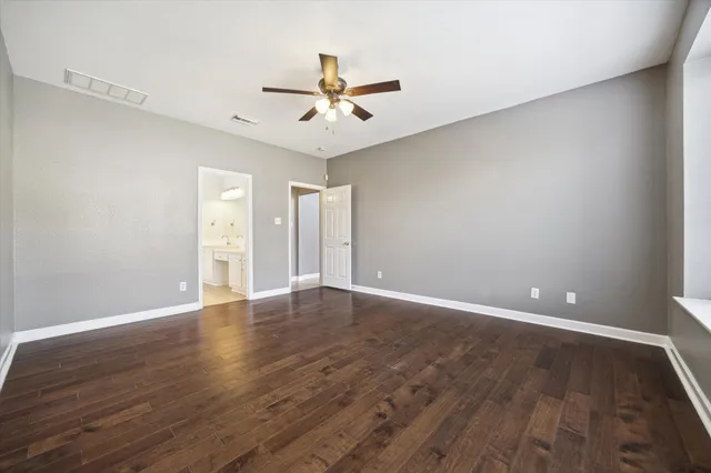a view of an empty room with wooden floor and a ceiling fan