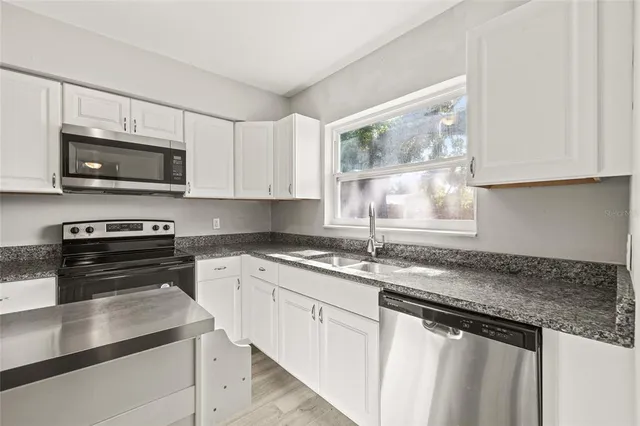 a kitchen with granite countertop a sink a stove top oven a counter space and cabinets