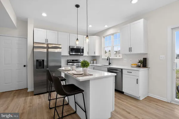 a kitchen with stainless steel appliances kitchen island granite countertop a sink a stove a refrigerator and white cabinets with wooden floor