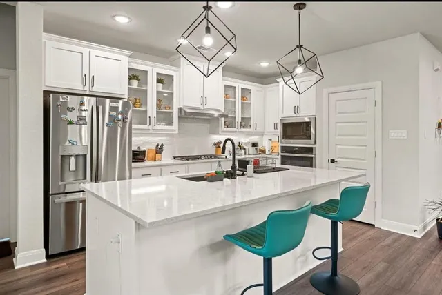 a kitchen with stainless steel appliances kitchen island granite countertop a refrigerator a stove a sink dishwasher and white cabinets with wooden floor