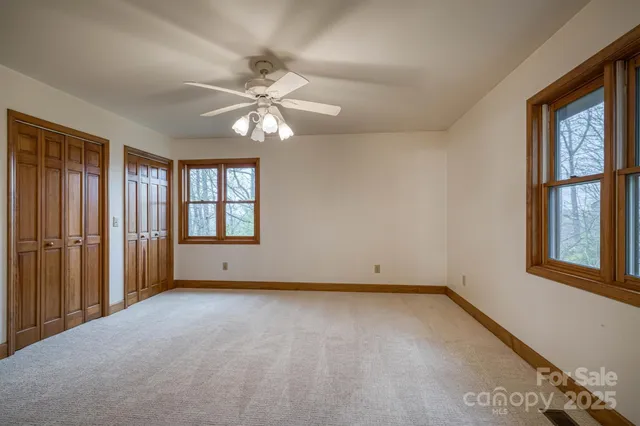 an empty room with chandelier fan and windows
